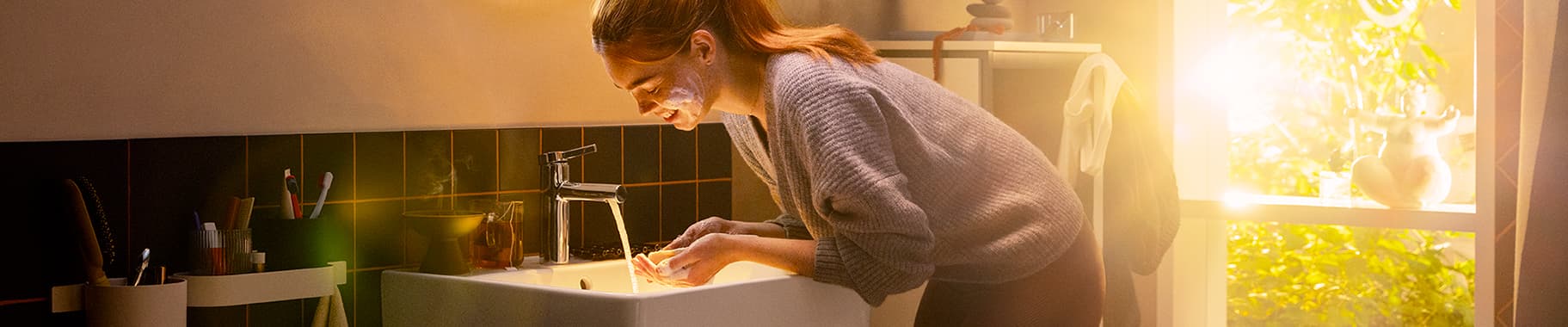 Mujer lavándose la cara con una griferĂa de lavabo hansgrohe Zesis S en cromo